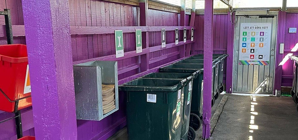 Soprum med lila väggar och gröna sopkärl